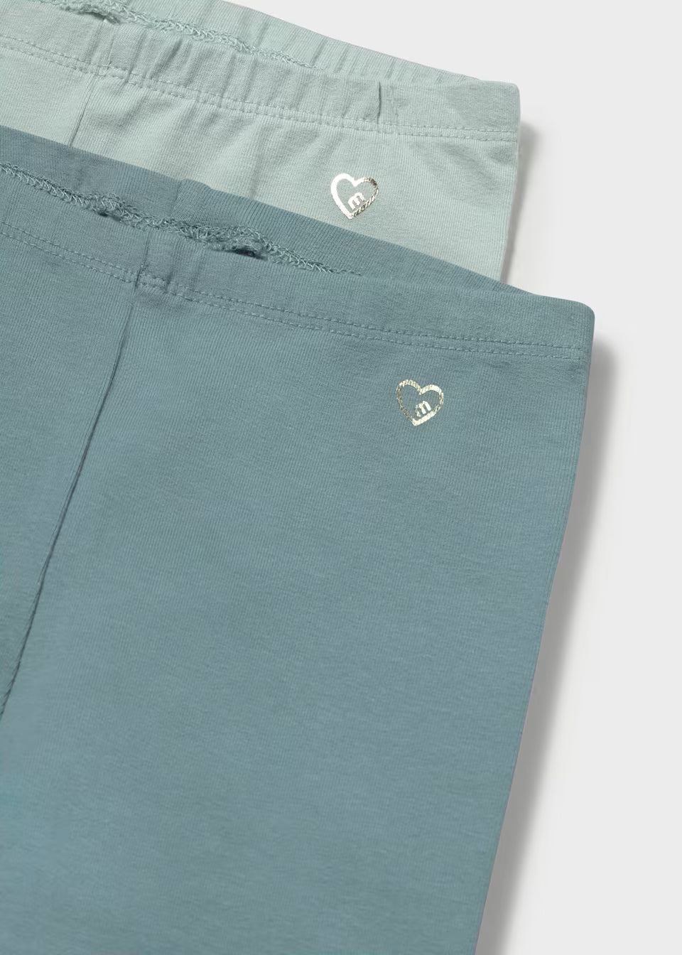 2-pack of girls’ cotton leggings in light and dark teal, each with a shiny heart near the waistband. Available in sizes 2T-6X.