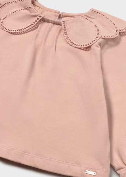 Light pink long-sleeve shirt with scalloped embroidered petal collar, eyelet trim, and small metallic tag at bottom hem. Available in sizes 2T-6.