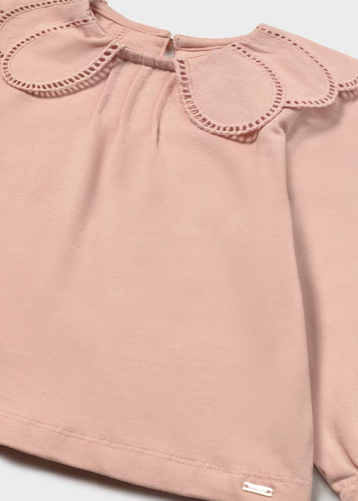 Light pink long-sleeve shirt with scalloped embroidered petal collar, eyelet trim, and small metallic tag at bottom hem. Available in sizes 2T-6.