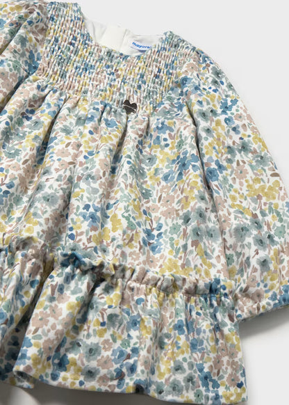 Baby Girl Floral Printed Velvet Dress with long sleeves, ruffled hem, smocked bodice, soft pastel blue, yellow, and beige floral print; velvety fabric; neckline tag detail. Available in sizes 0-3M to 24M.