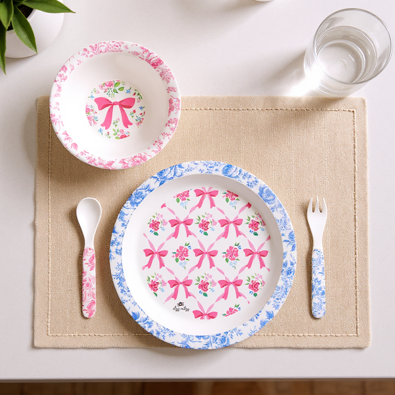 Itzy Bistro™ 4-Piece Set: BPA-free bowl, plate, spoon, fork; pink bows/floral on beige placemat. Sizes: toddler & child.