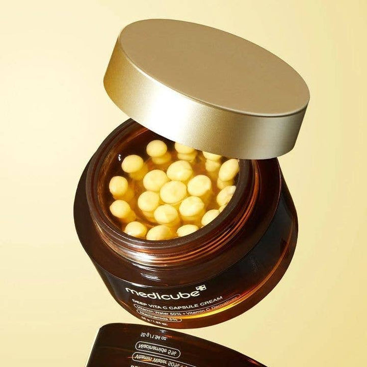 MEDICUBE Deep Vita C Capsule Cream in a brown jar with lid open, showing yellow cream inside. Available in 50ml and 20ml sizes.