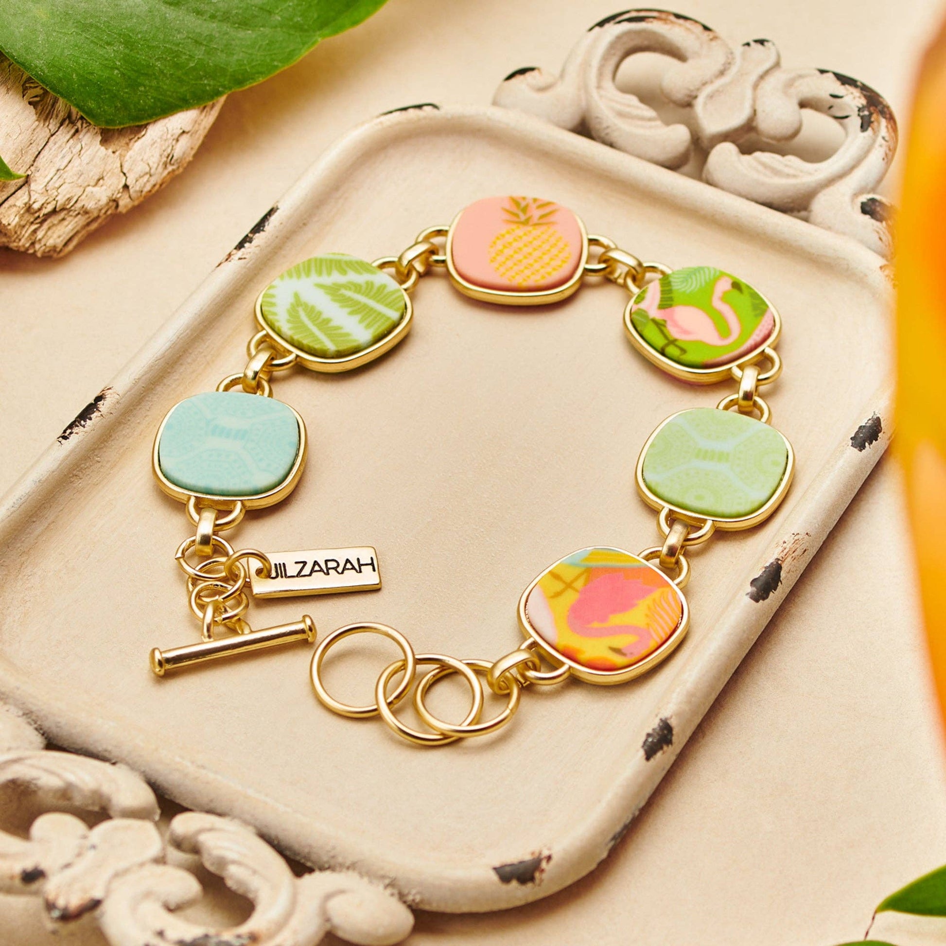 Palm Beach Reversible Coin Bracelet with six enamel tropical charms (pineapple, flamingo, palm leaves). Features brand tag "LIZARAH" near clasp. Available sizes: S/M and M/L.