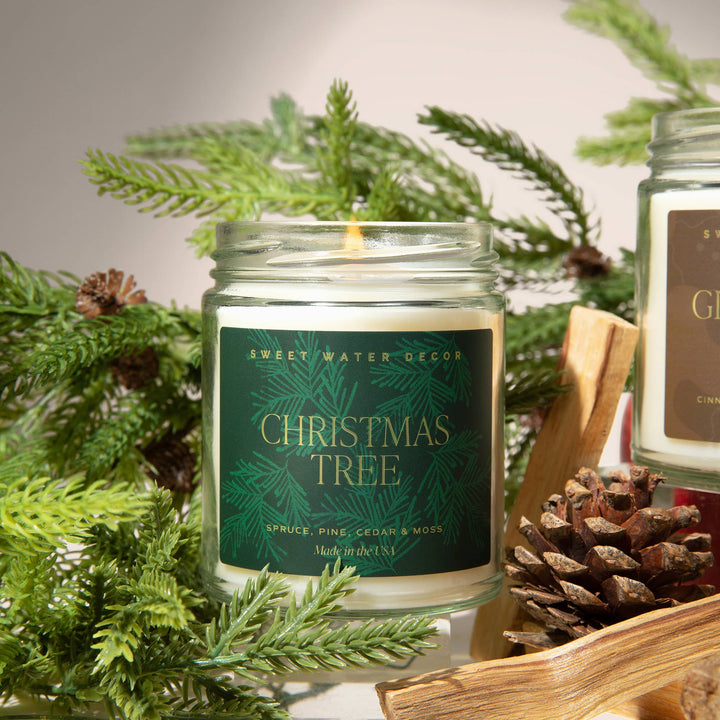 9 oz soy candle in a clear glass jar with a green label reading “Christmas Tree, Spruce, Pine, Cedar &amp; Moss.”