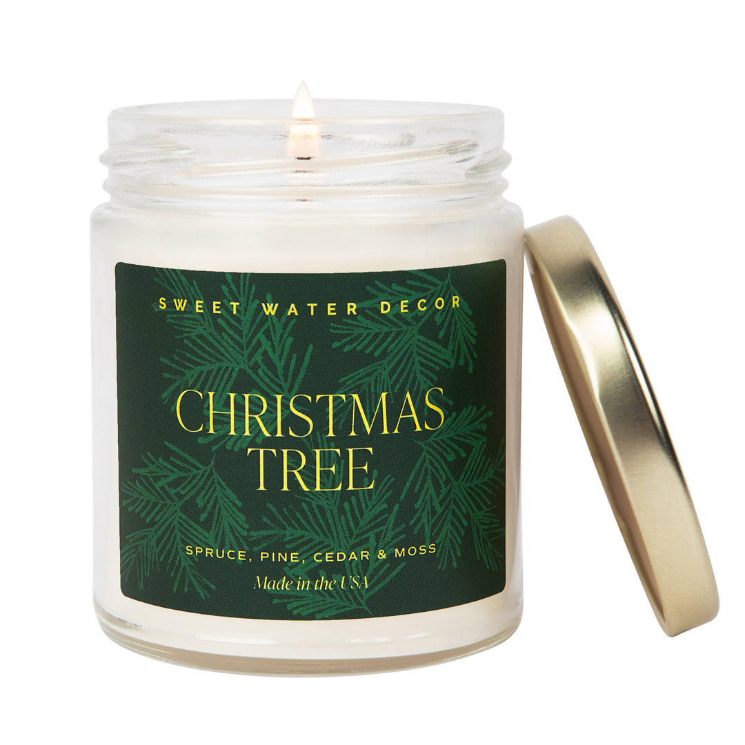 9 oz Christmas soy candle in a glass jar with a lit wick, gold lid, and pine-illustrated label.