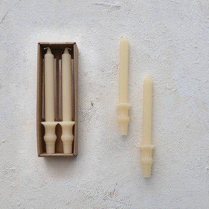 Brushed concrete background with set of 2 candles in box and set of 2 candles by themselves. Ivory candlesticks with urn bases