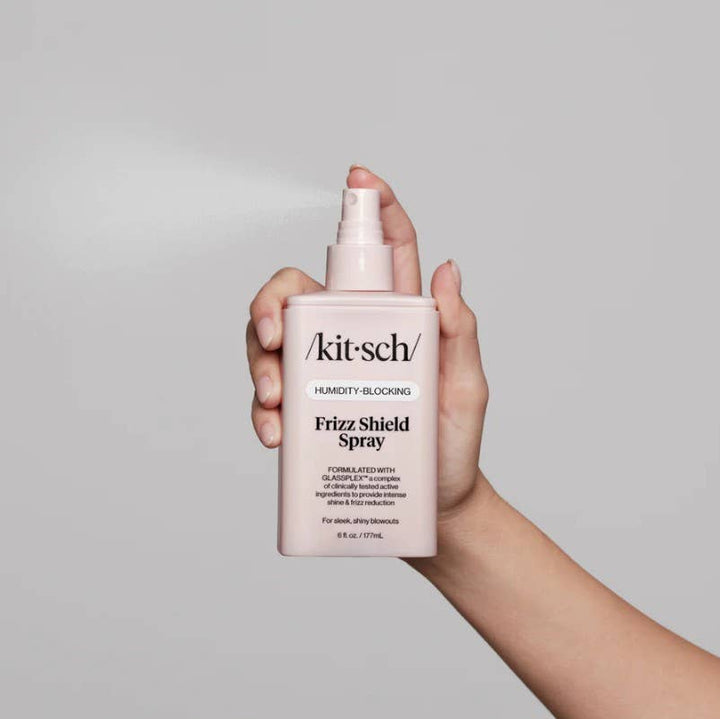 Humidity Blocking Frizz Shield Spray bottle emitting a fine mist.
