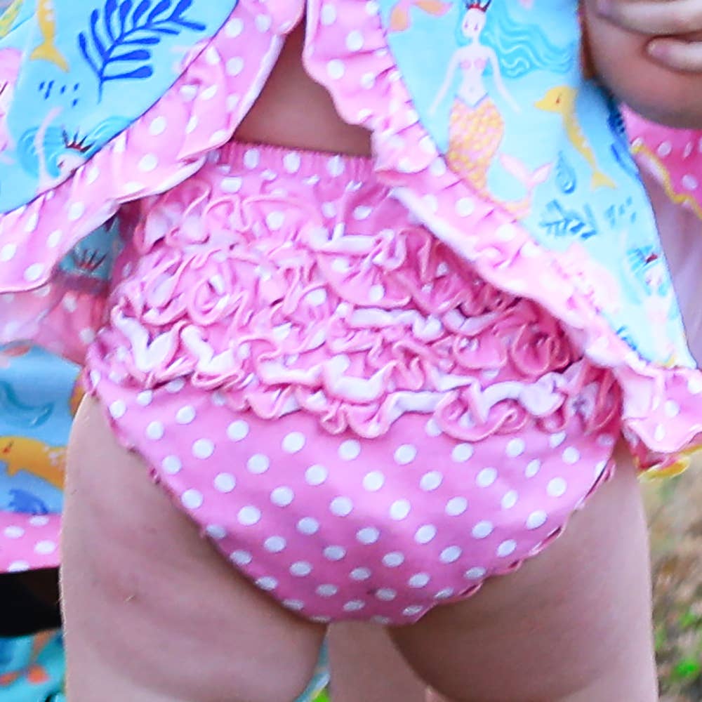 A close-up of a baby wearing a Pink Polka Dot Knit Ruffled Baby Bloomers: 12-24 mo, partially covered by a colorful blanket with a bird pattern.