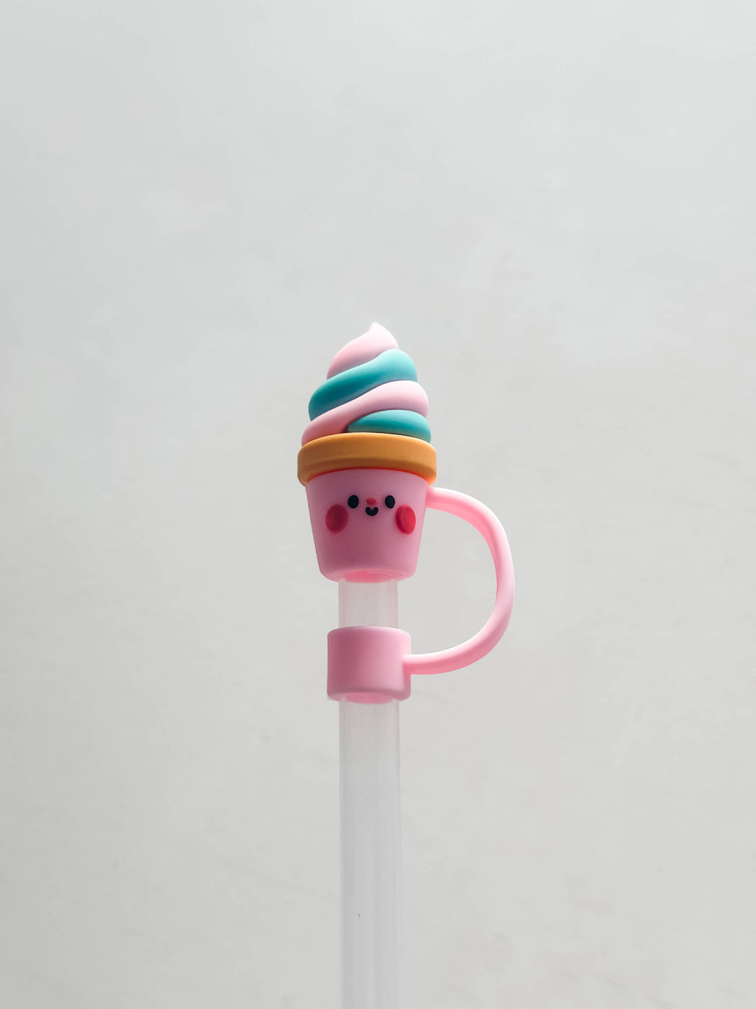 Silicone straw cover shaped like a smiling ice cream cone with pink cheeks and blue, white, and pink swirl. Available in standard size.