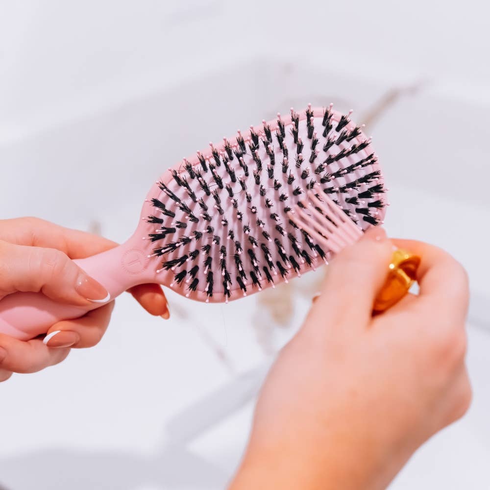 Oval Boar Brush in Bubblegum Pink being cleaned with a small tool.