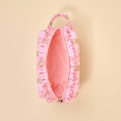 Small pink floral quilted pouch with ruffles, handle, zipper, and wipeable gingham interior. Available in one size.