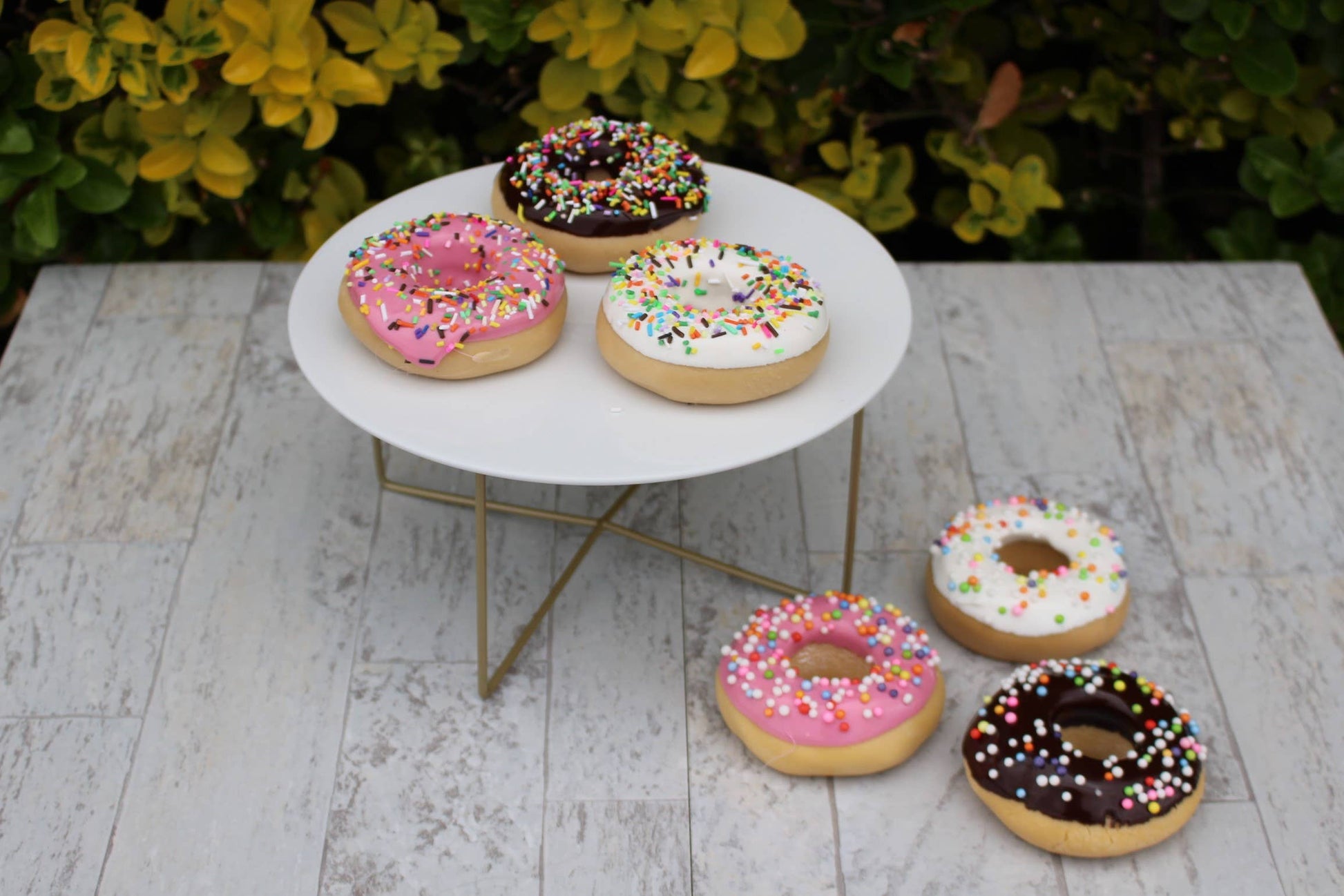 This product is a variety of Assorted Fake Donuts with sprinkles. Comes in different sizes and shapes, these faux donuts are highly realistic and adorned with colorful faux sprinkles. Displayed on a small round white table which is available for purchase separately.