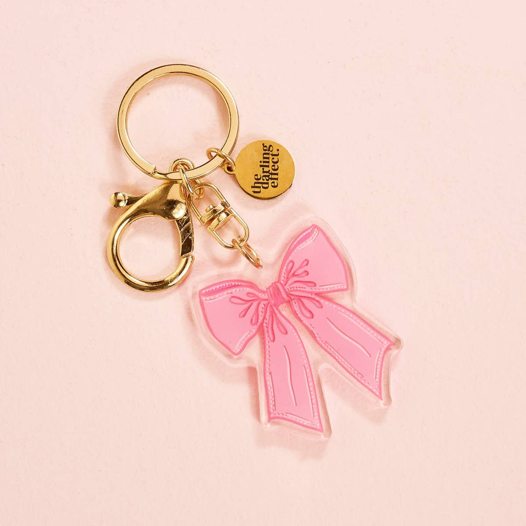 Gold acrylic keychain with clip, round tag reading "the ring cafe," and pink bow charm. Sizes available: not specified.
