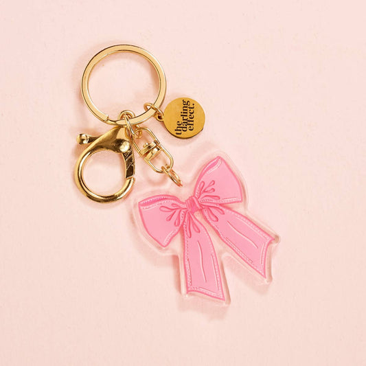 Gold acrylic keychain with clip, round tag reading "the ring cafe," and pink bow charm. Sizes available: not specified.
