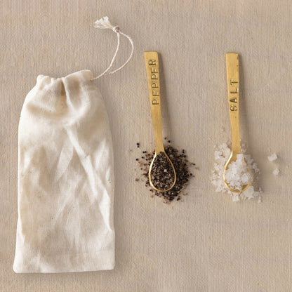 Set of two 3-1/4" metal spoons labeled "Salt" and "Pepper," brushed brass finish. Includes white drawstring pouch.
