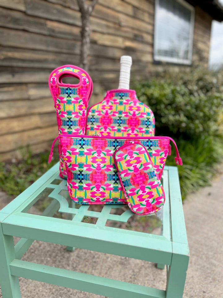 The Laura Park Pink Paradise Wine Sleeve is displayed on a mint green table. Available sizes: standard and large.