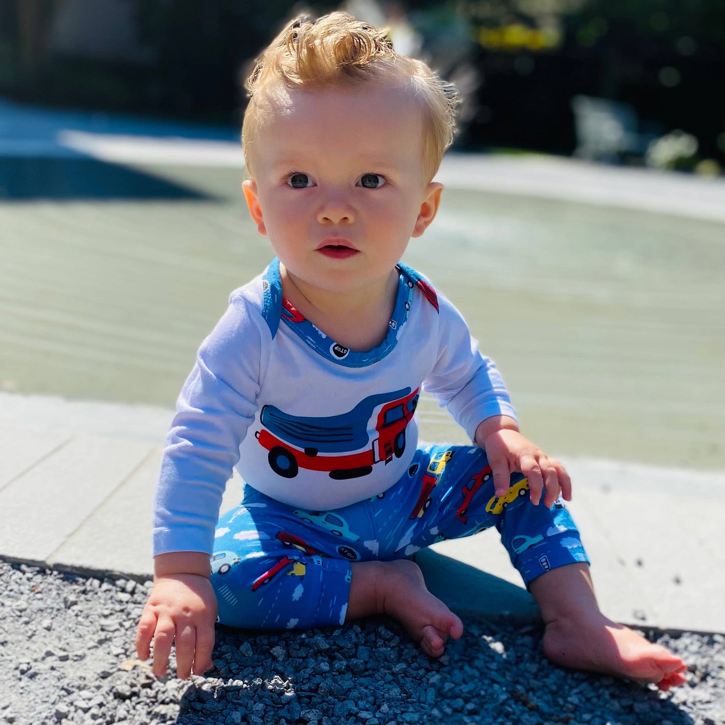 Little boy modeling onesie and pants sitting on ground.