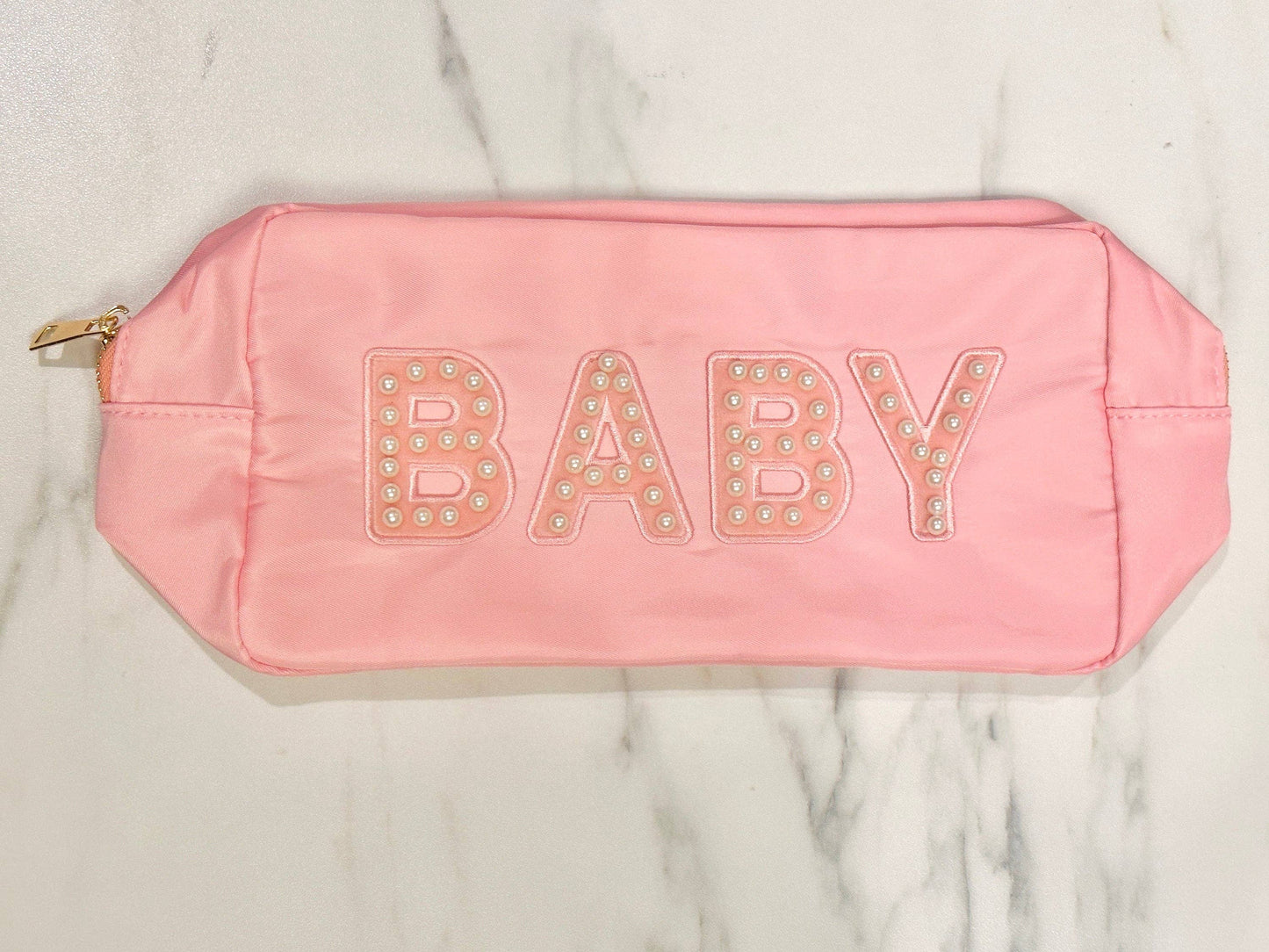 Pink nylon bag with "BABY" in pearl-adorned letters. Features a smooth texture and gold zipper pull. Sizes: Small, Medium, Large.