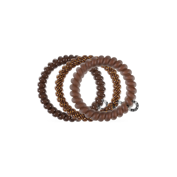 Three waterproof Morning Brew Small Hair Ties in brown tones, each with a unique texture—smooth, matte, and braided with gold accents—plus a silver tag. Available in small size. No-crease, gentle on hair.