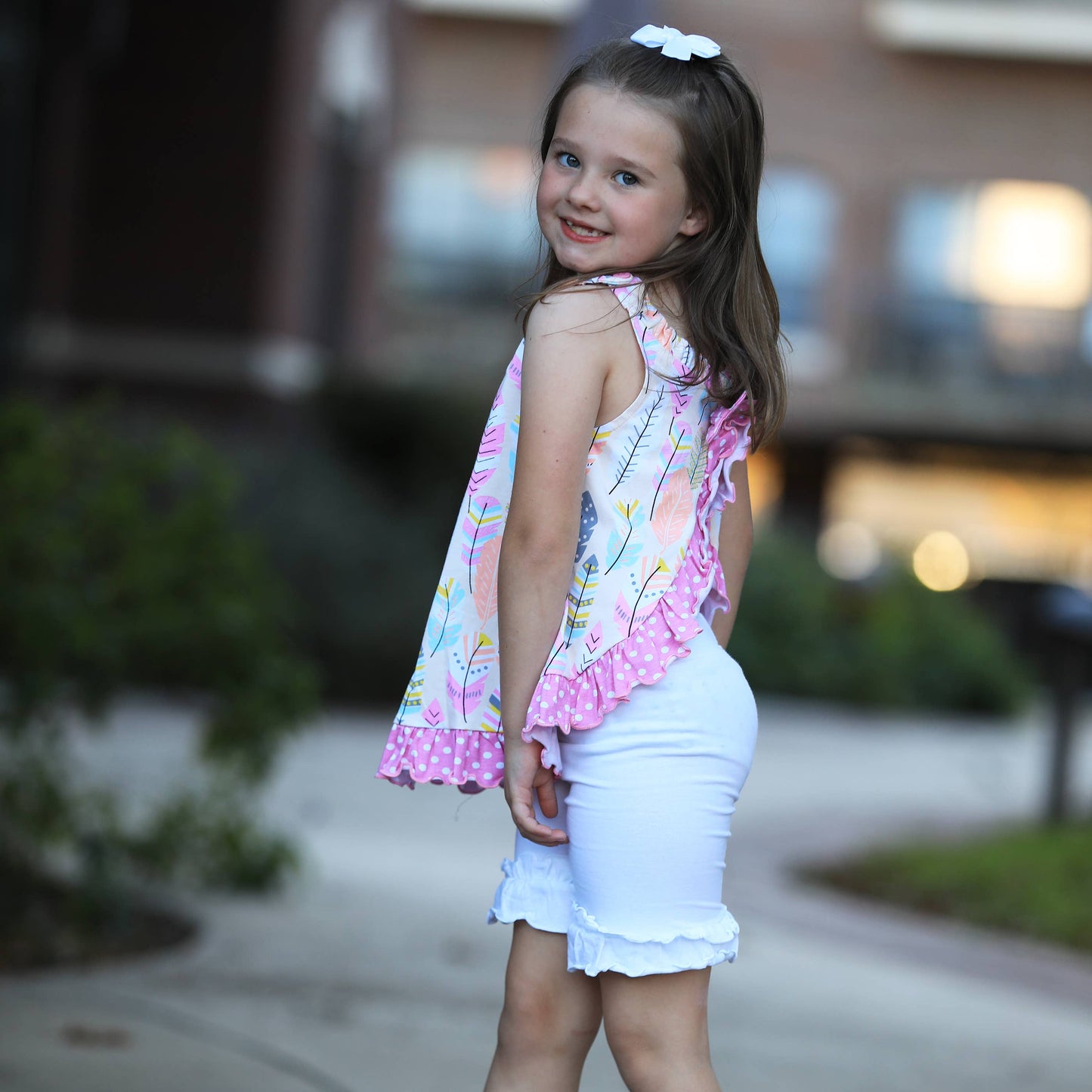 Young girl modeling top with white ruffle shorts (not included). She has a white bow in her hair.