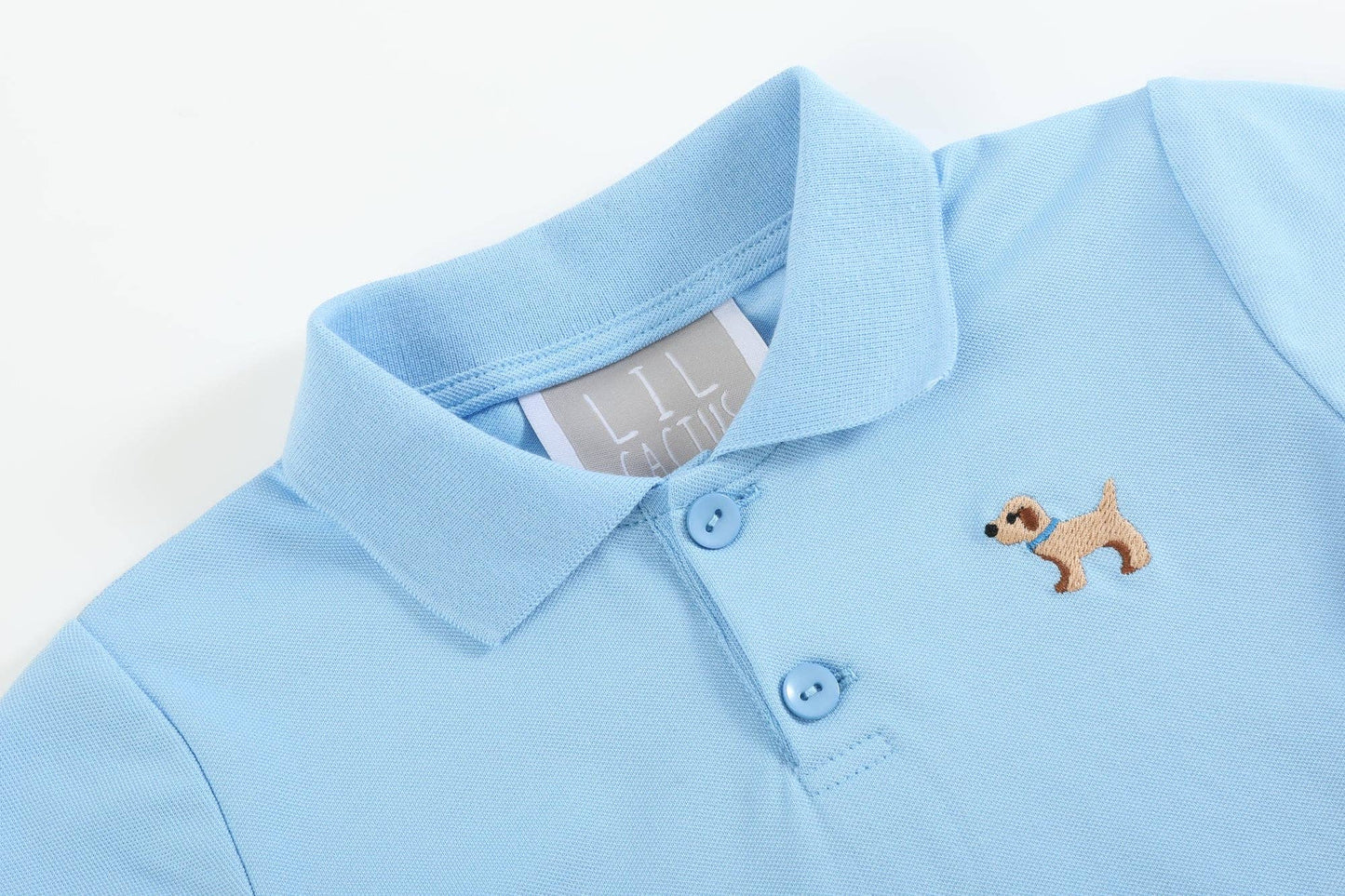 Light blue polo shirt with collar, two buttons, dog with sunglasses patch; white inner tag. Sizes: XS, S, M, L, XL.