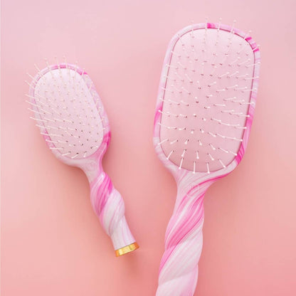 “Mini Detangler Brush | Medium | Pinch Me!” hair brushes in pink and white, with twisted handles, white bristles tipped in pink, and gold accents at the handle base. Available in medium size.