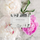 This Vintage Peony Soap is a bath bar presented in beautiful floral paper wrapping. It carries the delicate scent of lush white and pink peony flowers. The soap has been crafted to capture the aesthetic of a vintage era, resting against an elegantly polished marble surface. The product is available in standard soap bar size.