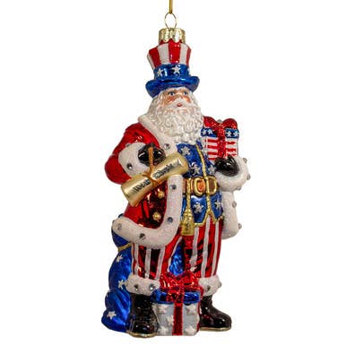 Bellissimo Glass Patriotic Santa Ornament in red, white, and blue with stars and stripes, holding a scroll and present; available sizes: 5" and 7".