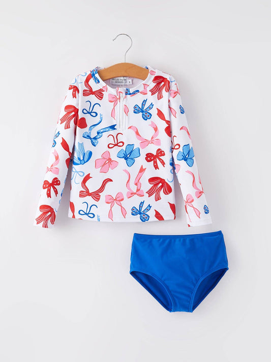 Kids’ two-piece swimsuit with long-sleeve white top featuring colored bows and blue bottoms. Sizes: 2T-6X.
