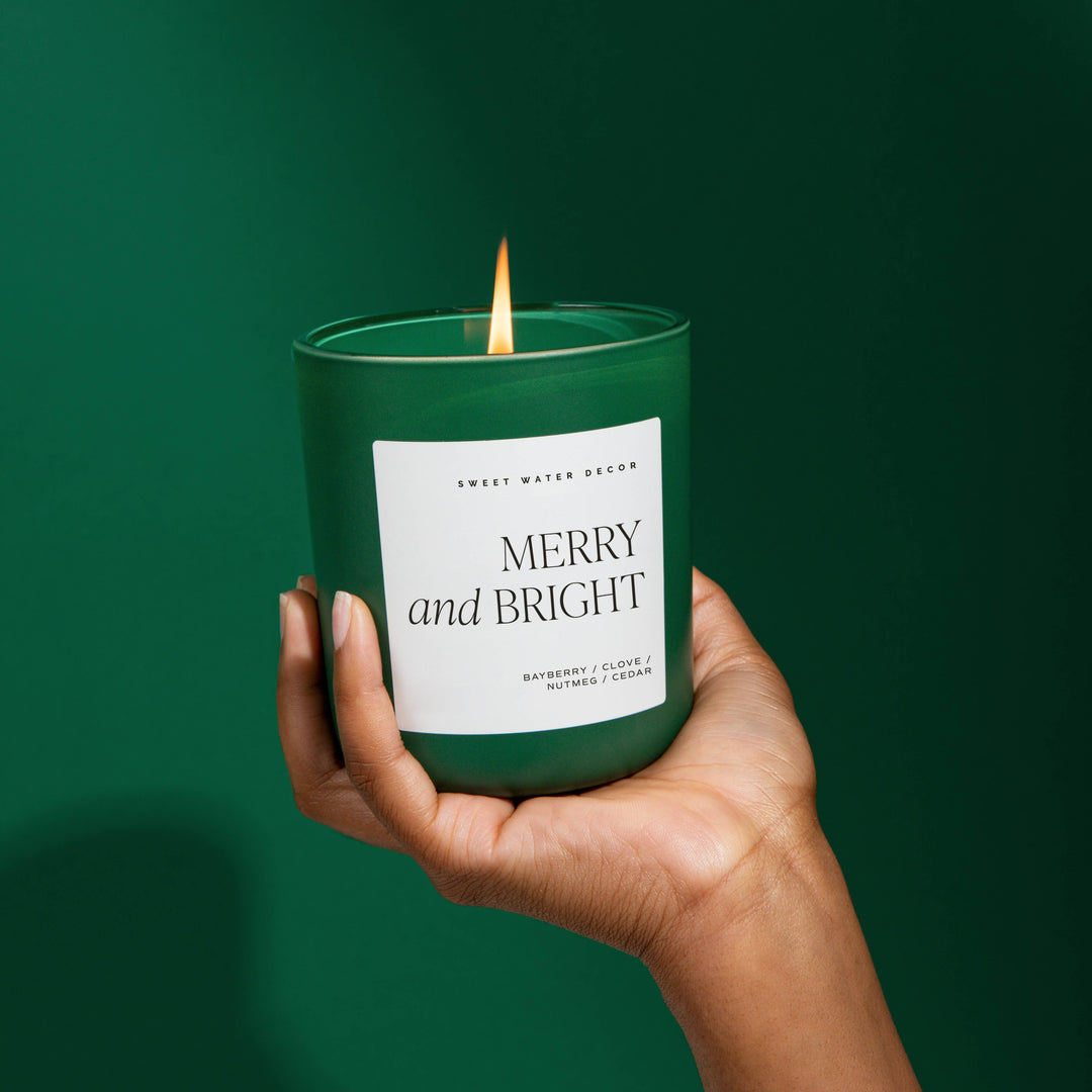 Matte green Merry and Bright 15 oz soy candle with a lit wick.