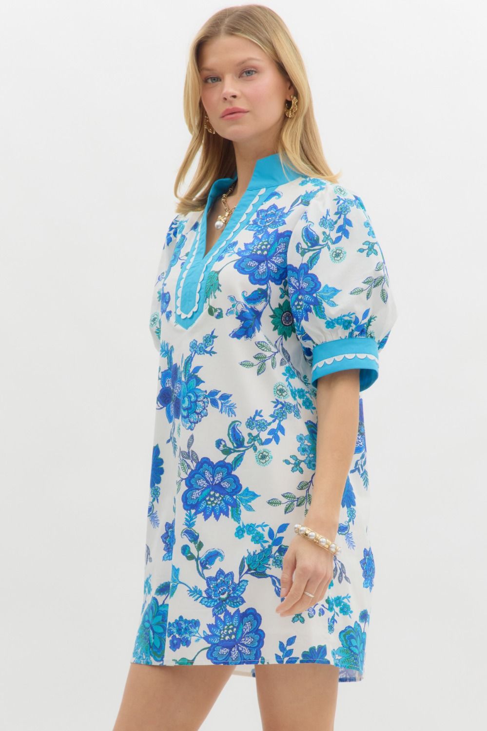 Blue Blossom Caftan Mini Dress features an A-line silhouette with blue floral designs and turquoise trim. Available in sizes XS–XL.
