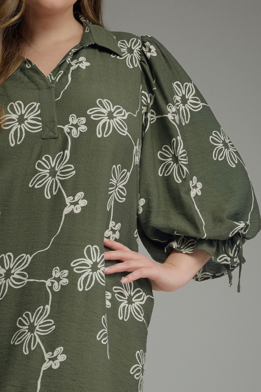 Olive Bloom Tie Waist Dress with olive green floral print, white patterns, tie waist, and balloon sleeves. Available in sizes XS-XL.
