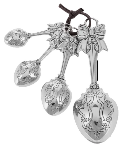 Set of four measuring spoons with ornate bow handles, sizes 1 tbsp, 1 tsp, ½ tsp, ¼ tsp, linked by a brown leather cord.