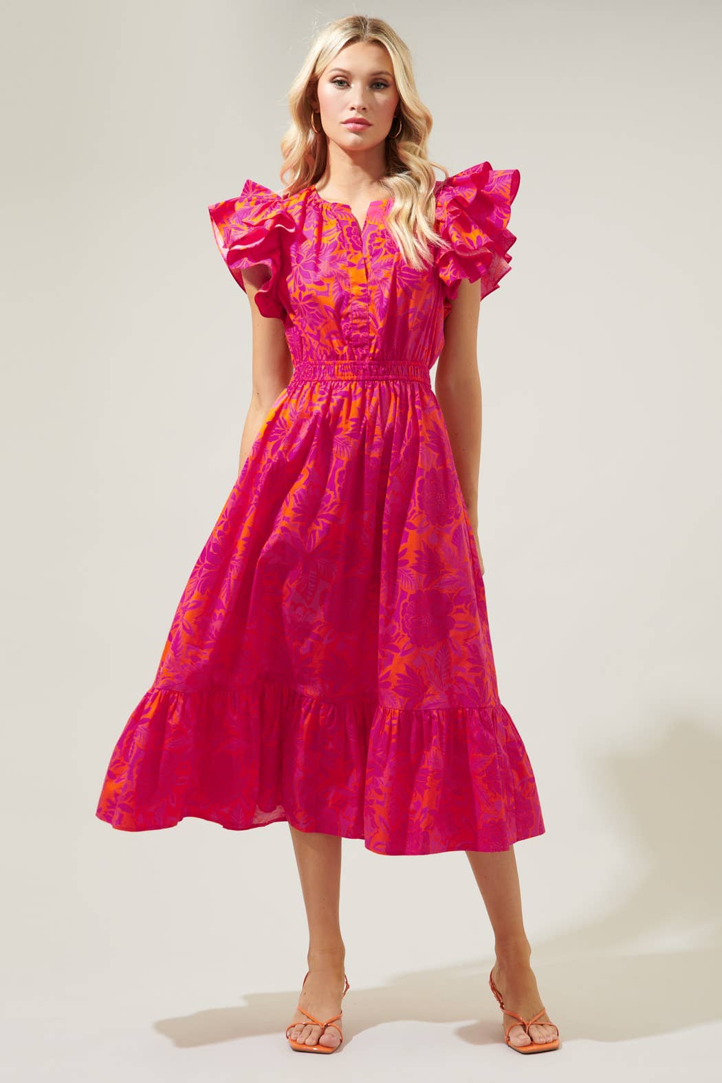 The Bali Tropics Jelina Ruffle Sleeve Midi Dress features vibrant pink and orange tropical print, ruffled sleeves and a tiered skirt. Available in women's standard sizes.