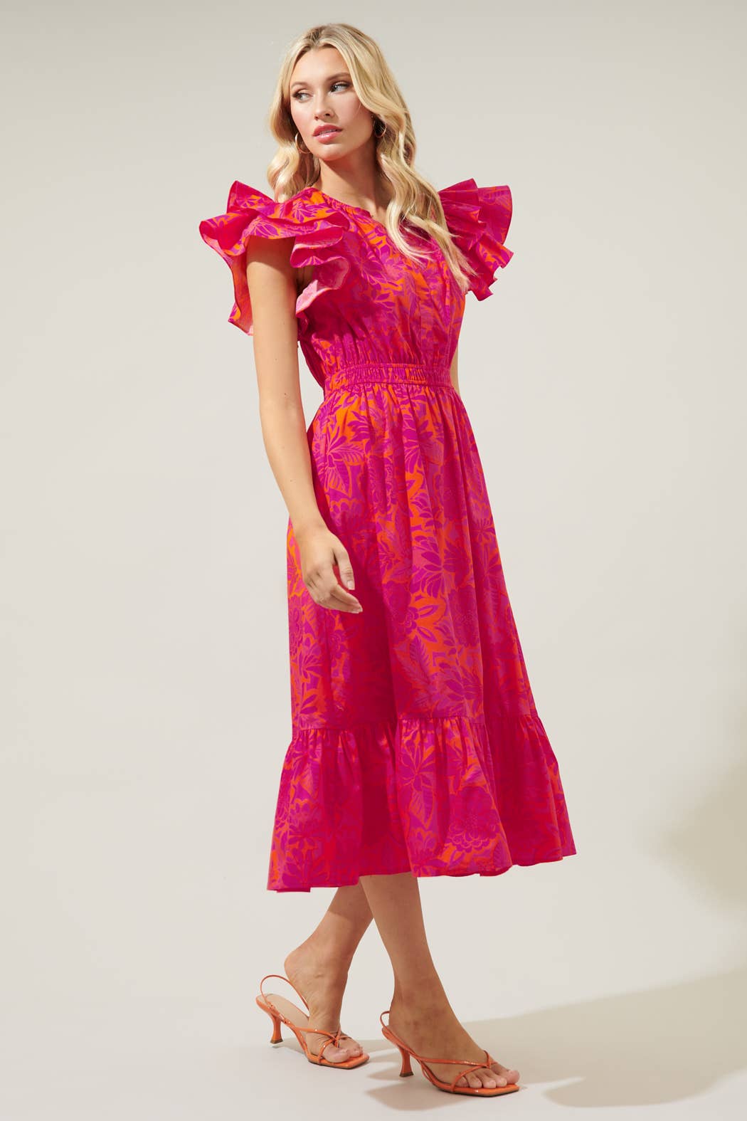 The Bali Tropics Jelina Ruffle Sleeve Midi Dress is a vibrant piece with a tropical pattern. It features a ruffle tier skirt for added style. Available sizes for this product range from small to extra large.