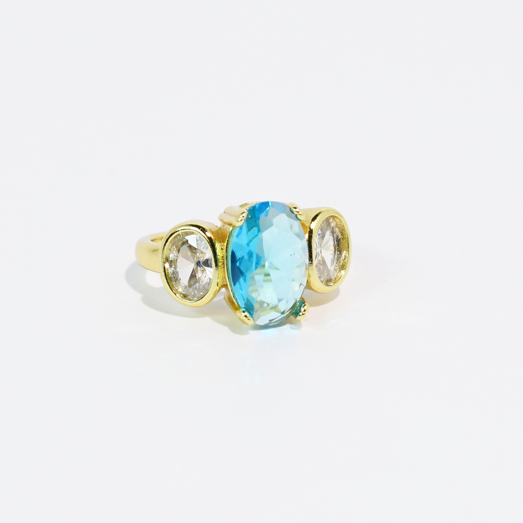 Gold ring with large oval aqua blue center stone, two smaller clear ovals each side. Available in sizes 5–9.
