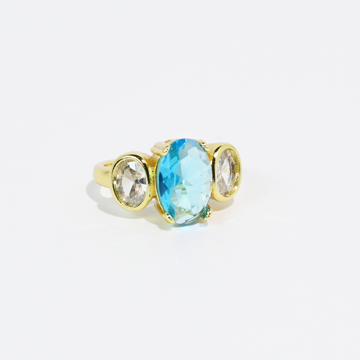 Gold ring with large oval aqua blue center stone, two smaller clear ovals each side. Available in sizes 5–9.