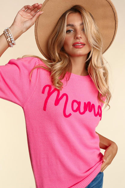 A stylish woman in a pink Mama Embroidered Pop Letter Short Bubble Sleeve sweater, touching the brim of her beige hat, posing elegantly with a slight tilt of her head.