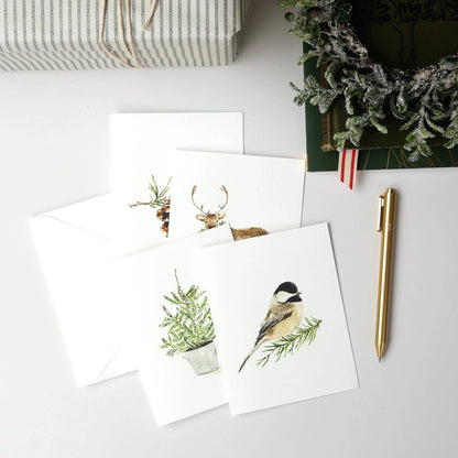 The Evergreen Christmas assorted notecard set includes four white watercolor cards with delicate animal and plant designs. Available in standard notecard size.