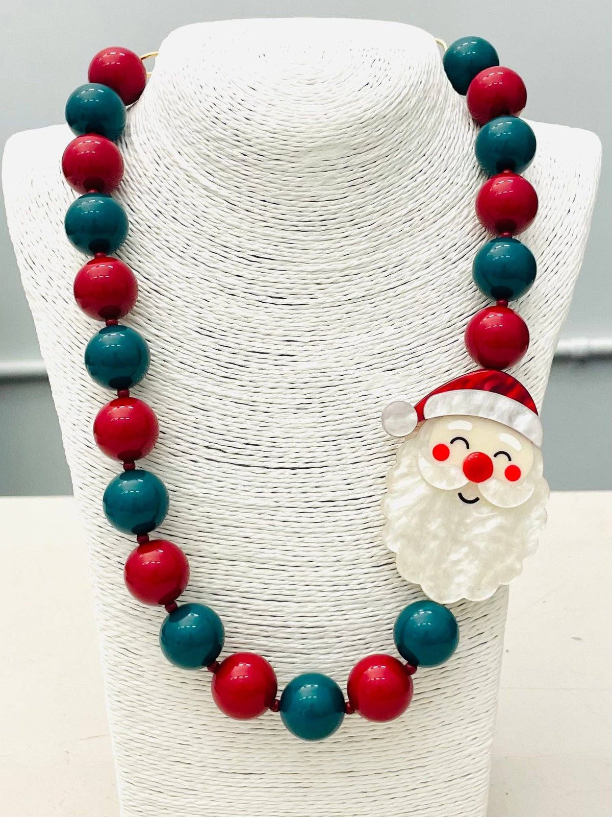 The HOLIDAY - Beaded Santa Necklace (red/green) BNK1213 has alternating red and green beads with a Santa Claus face charm on the right side. Sizes available: not specified.