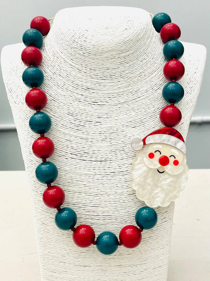 The HOLIDAY - Beaded Santa Necklace (red/green) BNK1213 has alternating red and green beads with a Santa Claus face charm on the right side. Sizes available: not specified.