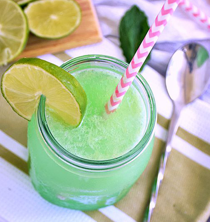 Glass of green lime drink with Wine & Cocktail Slush Mix Bags, topped with a lime slice and pink-striped straws. Available in 8oz, 16oz.