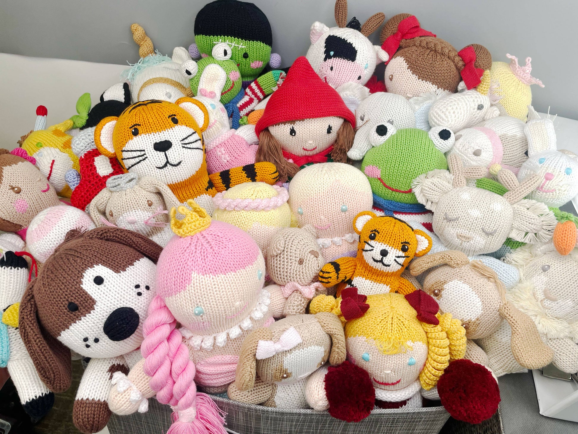 A large collection of colorful, handmade crochet stuffed animals, including figures of dogs, tigers, and Harriett the Bunny Knit Doll: 12" Plush dolls, piled together in a cozy heap.