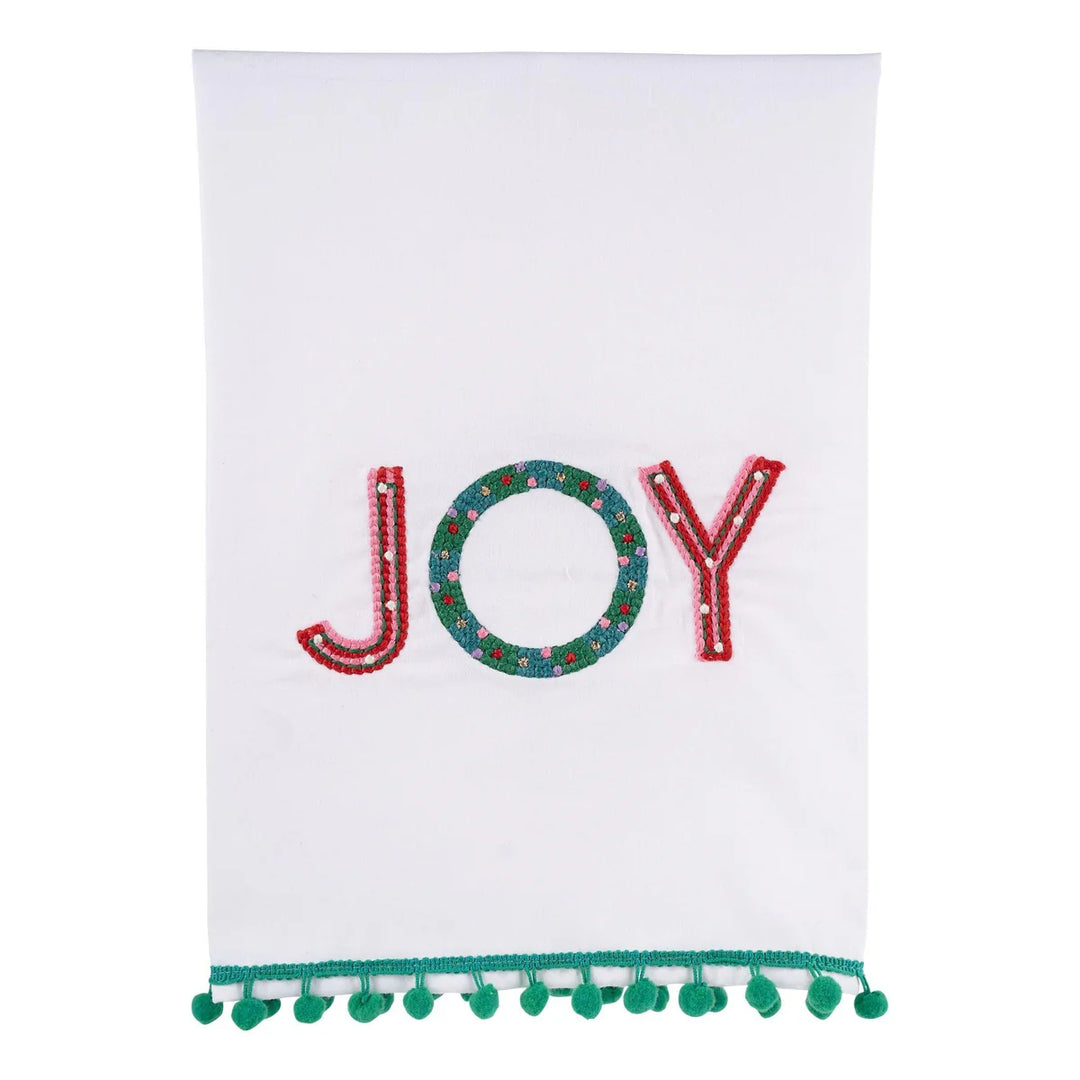 Bright Joy Tea Towel, white fabric with red and green “JOY” embroidery and green pom-pom trim.