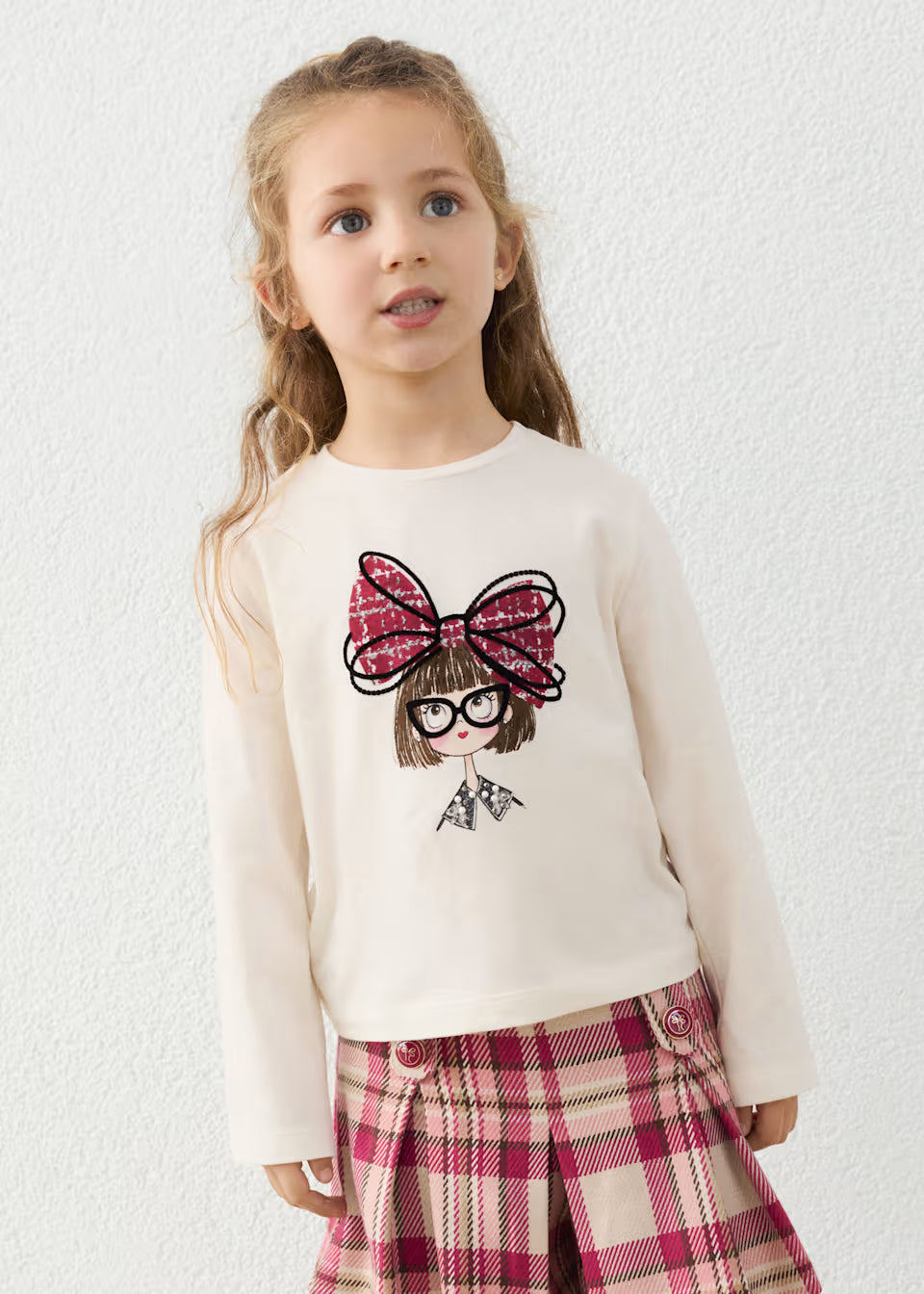 Little Girl Doll Long Sleeve T-Shirt with Bow in cream, features cartoon doll print and red plaid bow. Available in sizes 2T–6T.