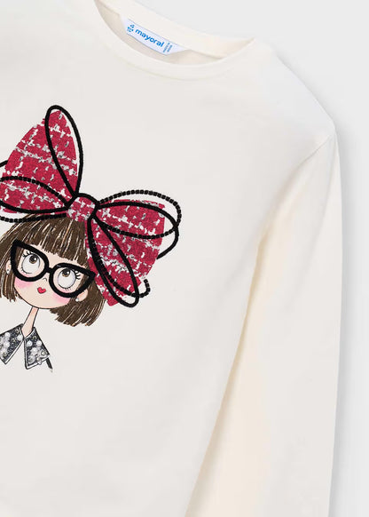 White long sleeve girls’ t-shirt featuring a cartoon girl print with short brown hair, black glasses, a red bow accent, and black-and-white outfit; includes subtle “Mayoral” label at neckline. Available in sizes 2-9 years.