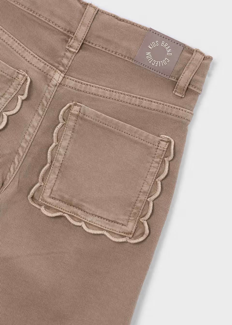 Tan Little Girl Twill Scallop Pants with textured twill fabric, visible stitching, wide-leg cut, scalloped back pocket, and brown waistband label with “KIDS BRAND COLLECTION” in white. Available in sizes 2T-6.