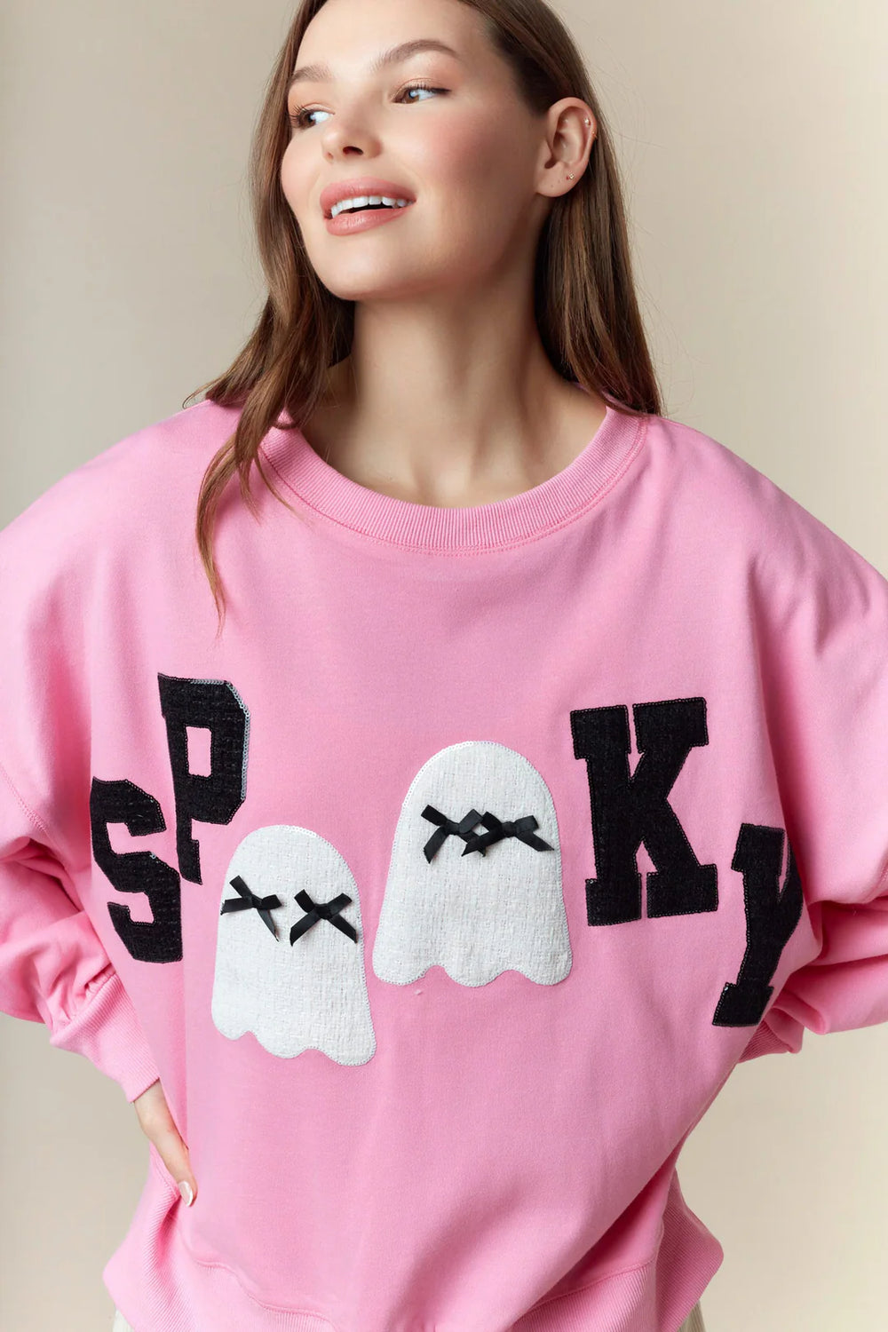 Spooky Boo Pink Patch Sweatshirt—oversized pink Halloween pullover with bold black “SPOOKY” text and two white ghost illustrations with closed eyes and lace patches at the center. Available in sizes S-XXL.