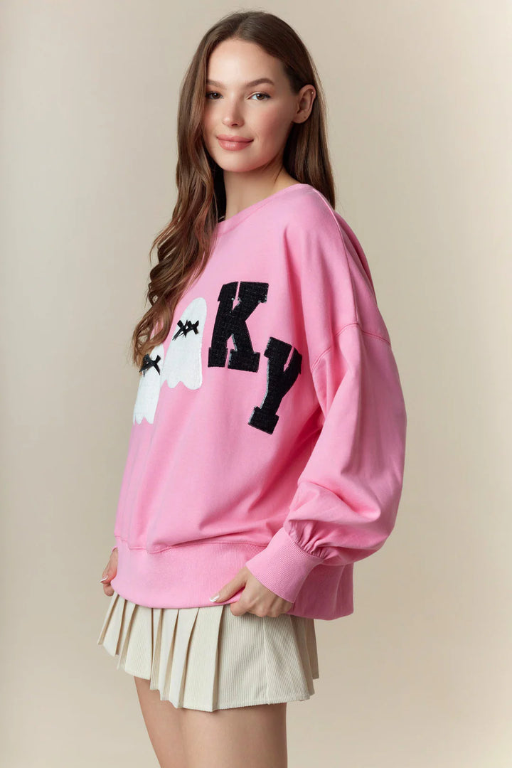Spooky Boo Pink Patch Sweatshirt: pink Halloween pullover with “SPOOKY” in black letters, white ghost faces, and lace ghost patches. Available in sizes XS-XXL.