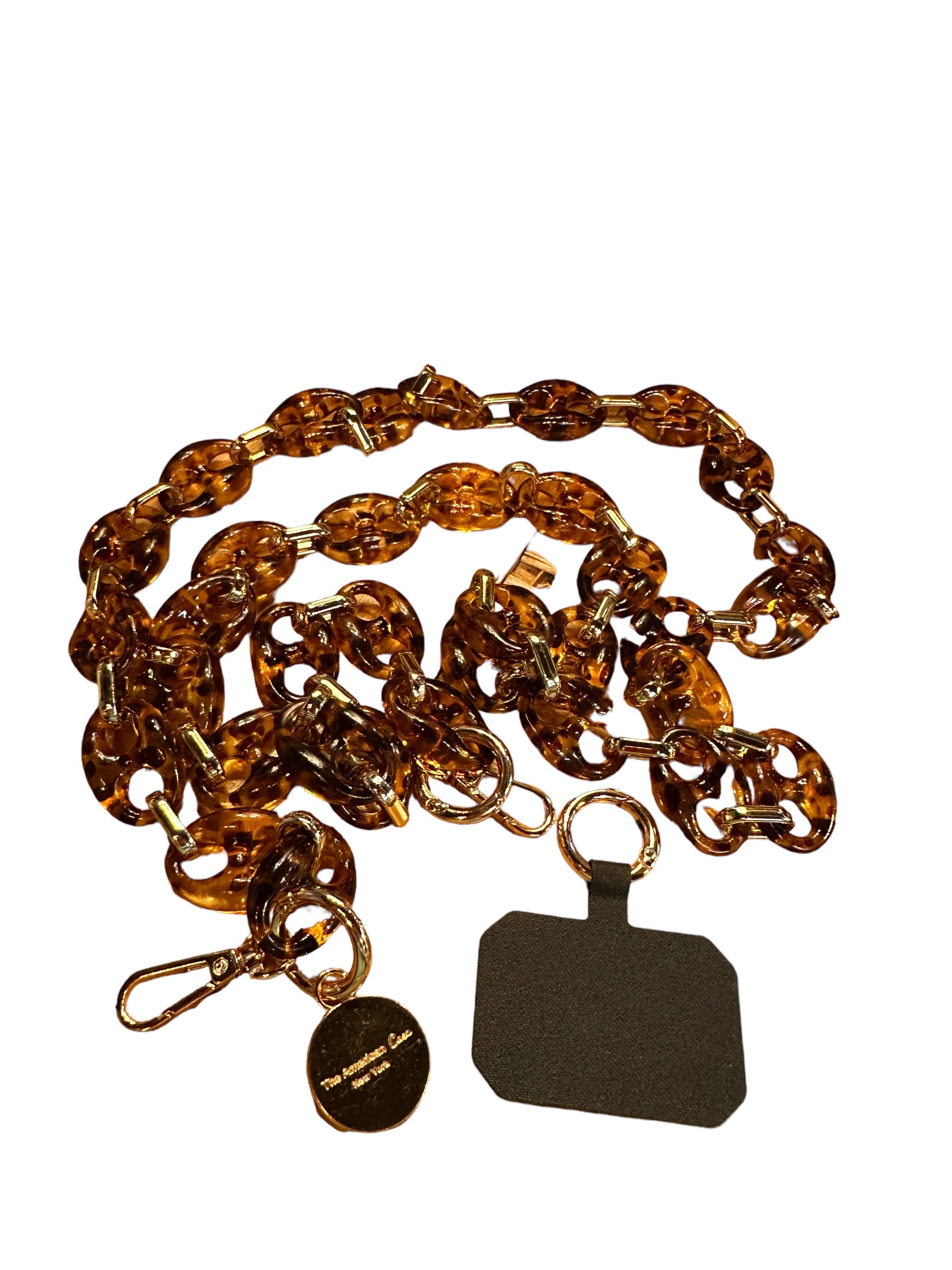 This is an acrylic chain featuring a tortoiseshell pattern. It comes with an adjustable crossbody phone strap and an attached rectangle black label. It allows for hands-free carrying of your phone. Product is isolated on white background. Available in one standard size, suitable for all types of smartphones.

